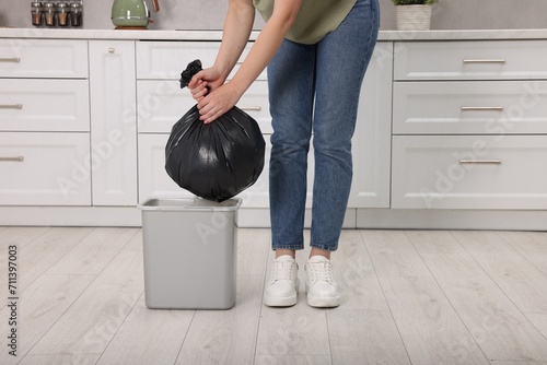 Woman taking garbage bag out of trash bin in kitchen, closeup