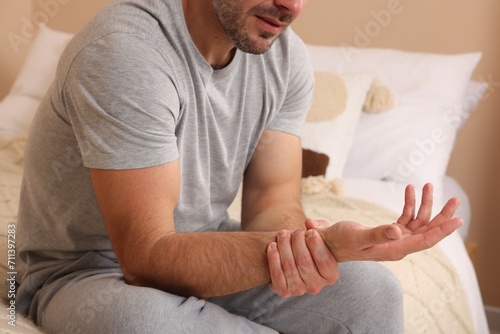 Man suffering from pain in his hand on bed indoors, closeup