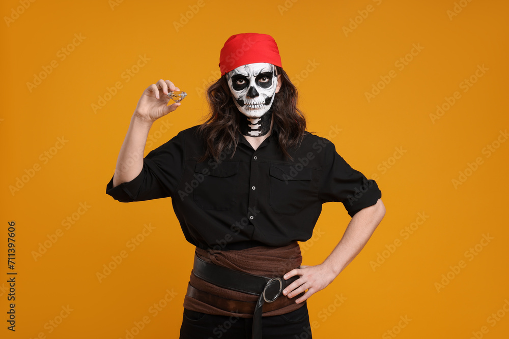 Man in scary pirate costume with skull makeup and gem on orange background. Halloween celebration