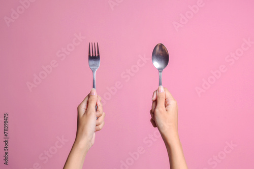Woman hands showing spoon and fork isolated on pink color pastel background photo