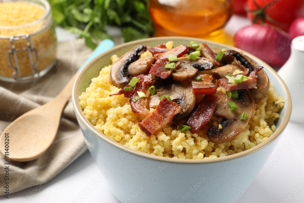 Tasty millet porridge with mushrooms, bacon and green onion in bowl on white table, closeup Tasty millet porridge with mushrooms, bacon and green onion in bowl on white table, closeup