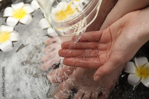 Woman pouring water onto hand while soaking her feet in bowl  above view. Spa treatment