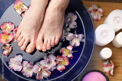 Woman holding her feet over bowl with water and flowers on floor, top view. Spa treatment