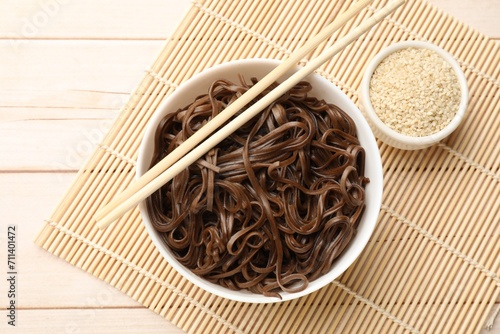 Tasty buckwheat noodles (soba) with sesame and chopsticks on wooden table, flat lay