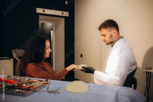 a woman holds a breast implant and talks to a plastic surgeon