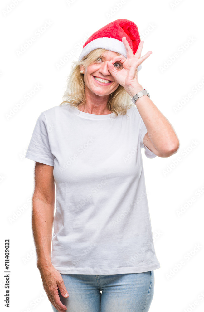 Middle age blonde woman wearing christmas hat over isolated background doing ok gesture with hand smiling, eye looking through fingers with happy face. Middle age blonde woman wearing christmas hat over isolated background doing ok gesture with hand smiling, eye looking through fingers with happy face.