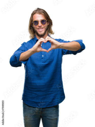 Young handsome man with long hair wearing sunglasses over isolated background smiling in love showing heart symbol and shape with hands. Romantic concept.
