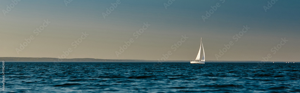 Sailing boat or yacht with open white sails floating on the sea at sunset. Majestic landscape, calm and tranquility