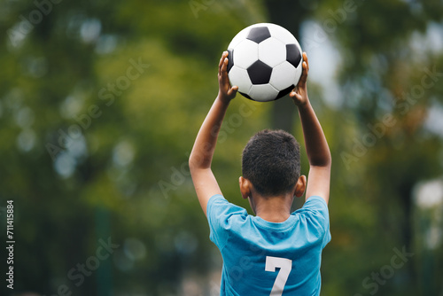Soccer Throw In During Children Sports Game. Little Boy Holding Soccer Ball in Hands. Kids Playing in Football League. Boy in Soccer Blue Jersey With Number Seven © matimix