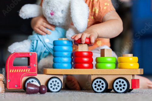Toddler placing coloured shape on correct peg of wooden toy truck photo