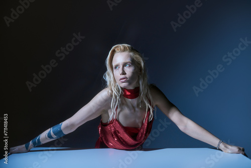 good looking stylish woman in red elegant dress sitting and looking away on dark background © LIGHTFIELD STUDIOS