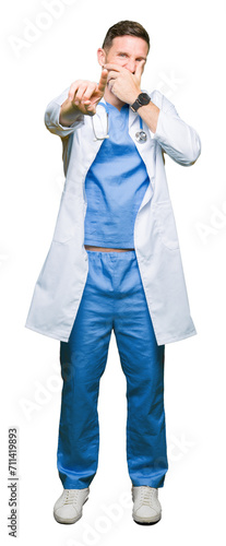 Handsome doctor man wearing medical uniform over isolated background Laughing of you, pointing to the camera with finger hand over mouth, shame expression