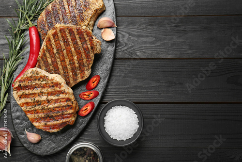Delicious grilled pork steaks with spices on dark wooden table, flat lay. Space for text