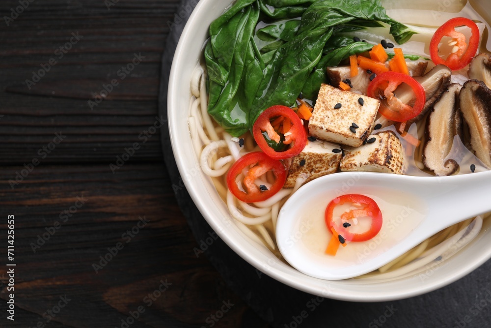 Bowl of vegetarian ramen and spoon on dark wooden table, top view. Space for text Bowl of vegetarian ramen and spoon on dark wooden table, top view. Space for text
