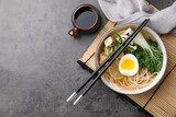 Bowl of vegetarian ramen, soy sauce and chopsticks on grey table, flat lay. Space for text