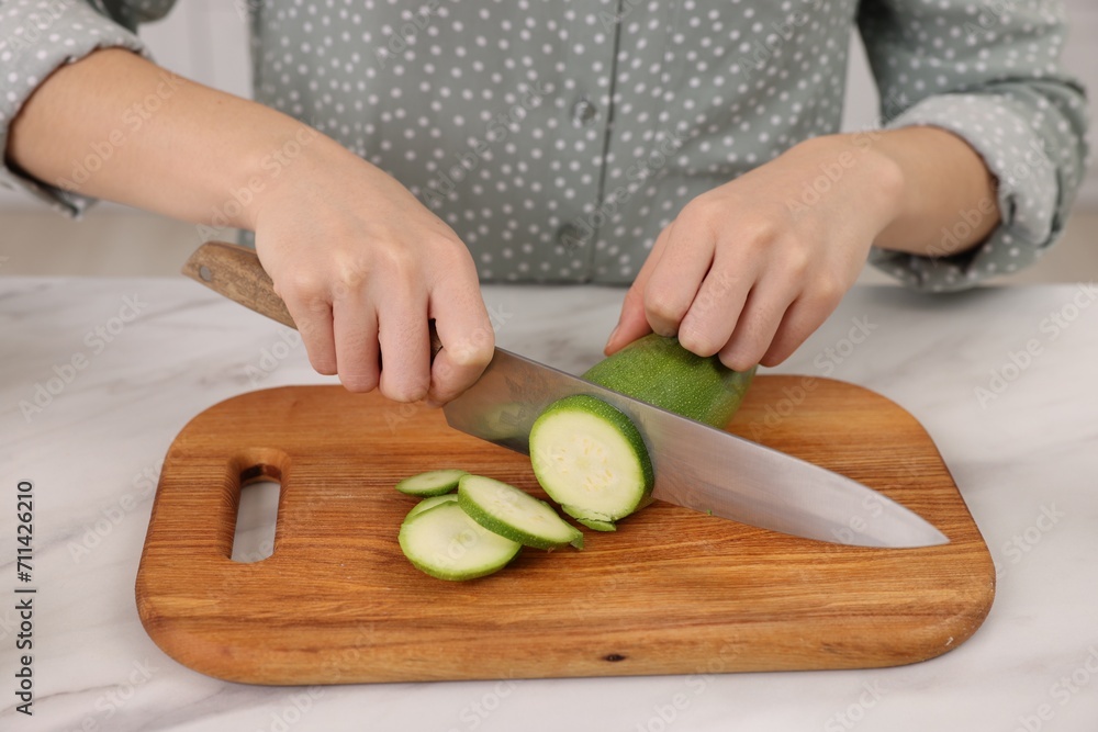 Cooking process. Woman cutting zucchini at white marble countertop, closeup Cooking process. Woman cutting zucchini at white marble countertop, closeup