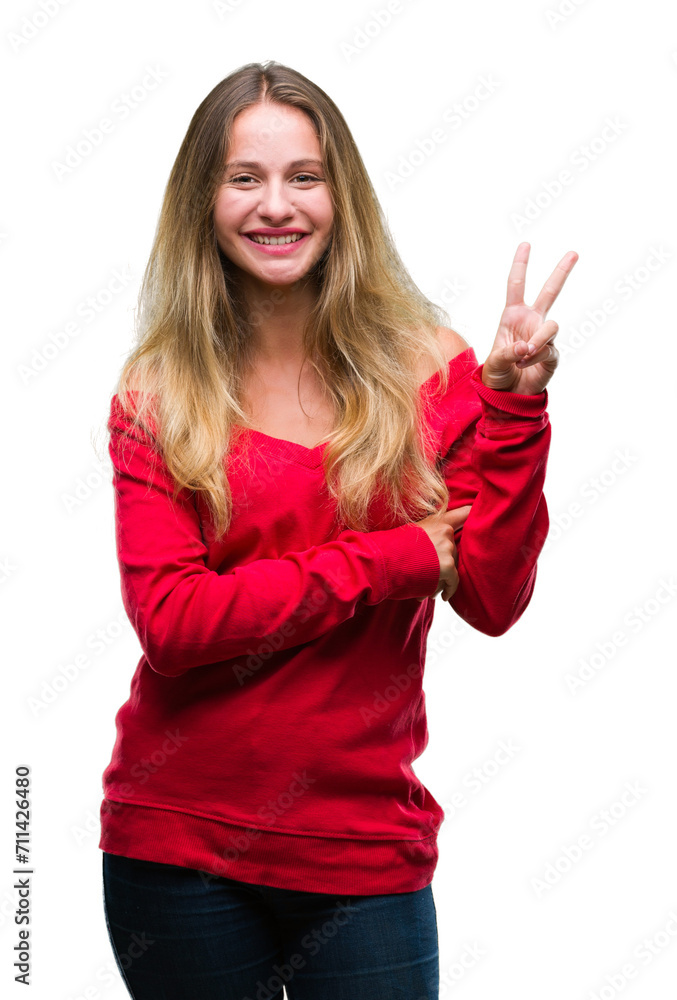 Young beautiful blonde woman wearing red sweater over isolated background smiling with happy face winking at the camera doing victory sign. Number two. Young beautiful blonde woman wearing red sweater over isolated background smiling with happy face winking at the camera doing victory sign. Number two.