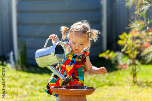 Toddler girl filling up bird bath with watering can in backyard photo