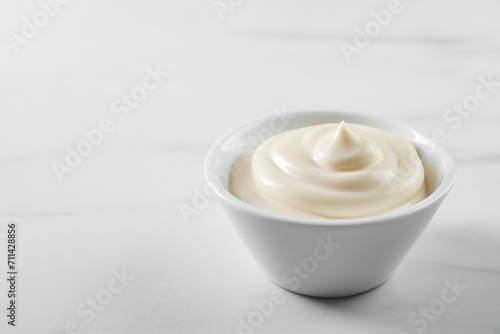 Tasty mayonnaise sauce in bowl on white table, closeup. Space for text