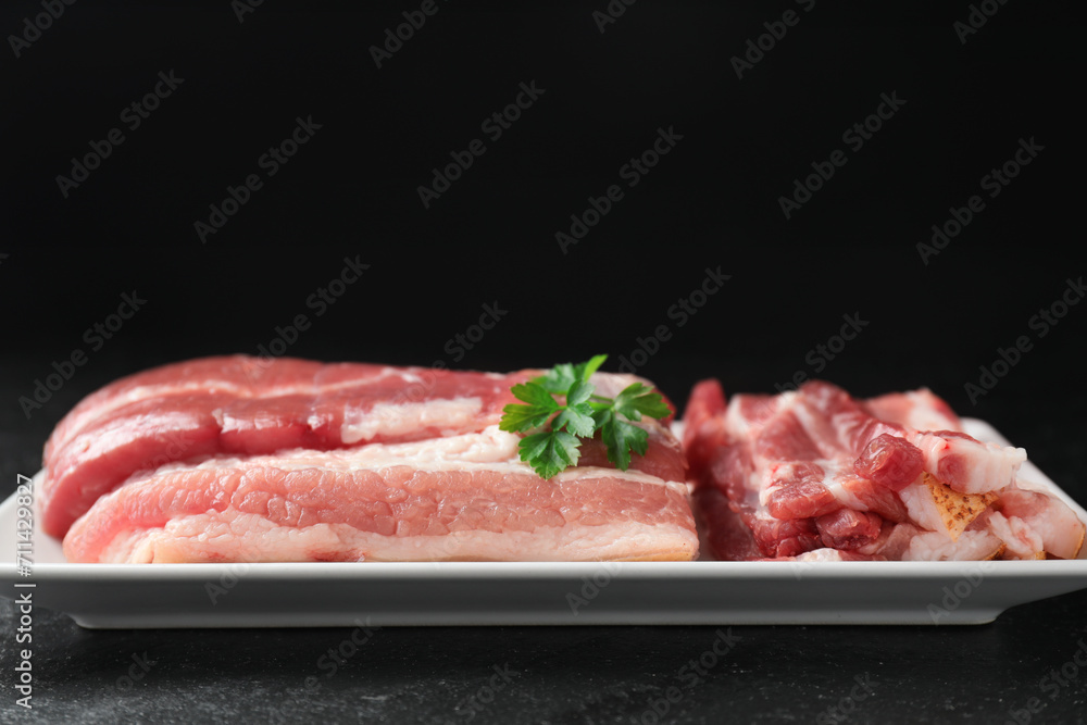 Pieces of raw pork belly and parsley on black textured table, closeup. Space for text Pieces of raw pork belly and parsley on black textured table, closeup. Space for text