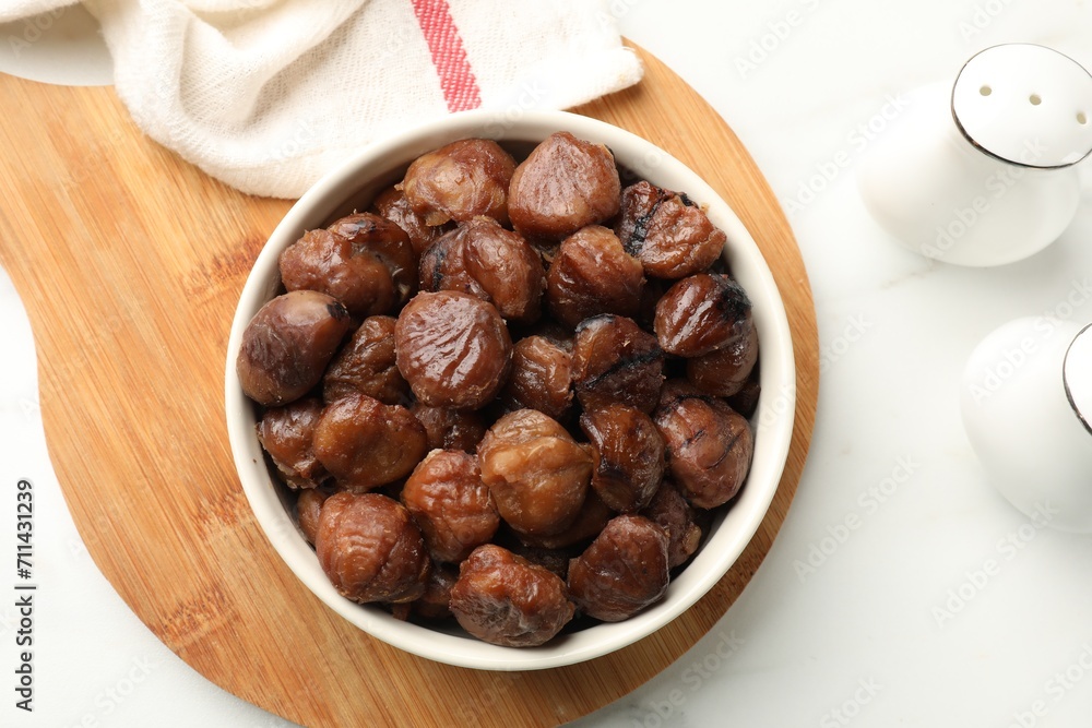 Roasted edible sweet chestnuts in bowl on white marble table, top view Roasted edible sweet chestnuts in bowl on white marble table, top view