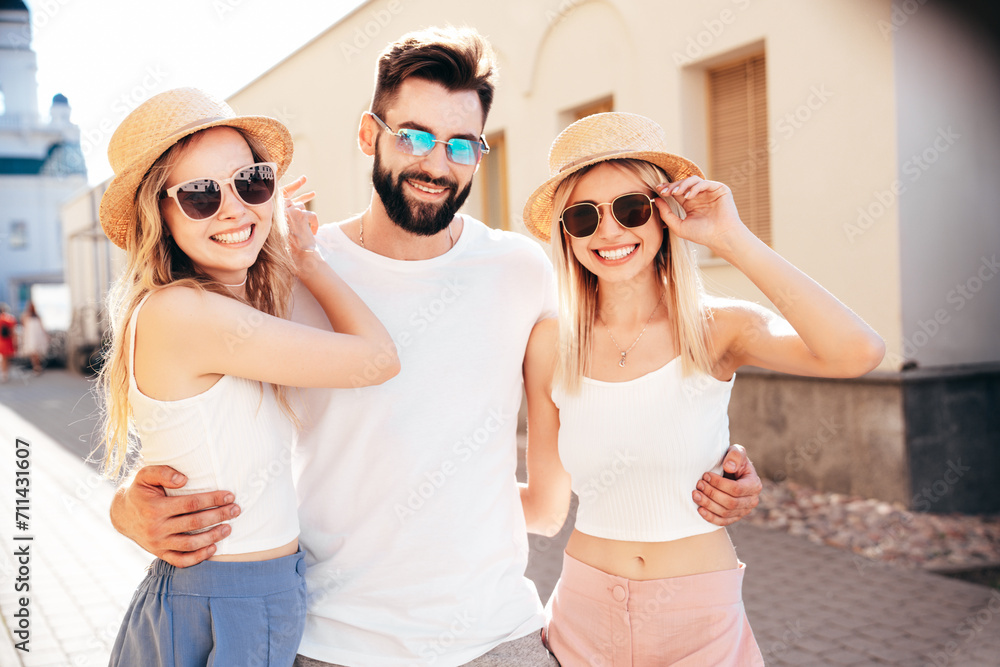 Group of young three stylish friends posing in the street. Fashion man and two cute female dressed in casual summer clothes. Smiling models having fun. Cheerful women and guy outdoors at sunny day Group of young three stylish friends posing in the street. Fashion man and two cute female dressed in casual summer clothes. Smiling models having fun. Cheerful women and guy outdoors at sunny day