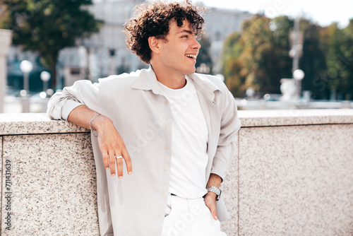 Portrait of young attractive man with curly hair hairstyle. Smiling handsome male in casual stylish clothes posing in the street at sunny day. Cheerful and happy model outdoors