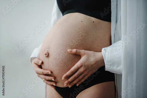 Closeup belly of a woman. Pregnancy motherhood procreation concept. Pregnant woman. Female waiting for newborn baby. Young pregnant girl touching and holding her belly and caring about health indoors.