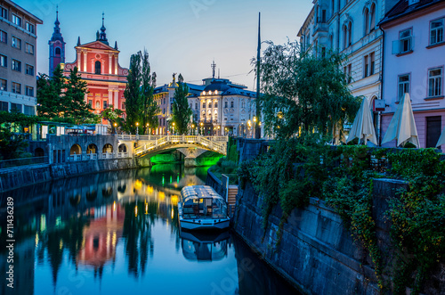 Twilight view of a calm river passing through Ljubljana, with illuminated historical buildings and a bridge reflecting on water photo