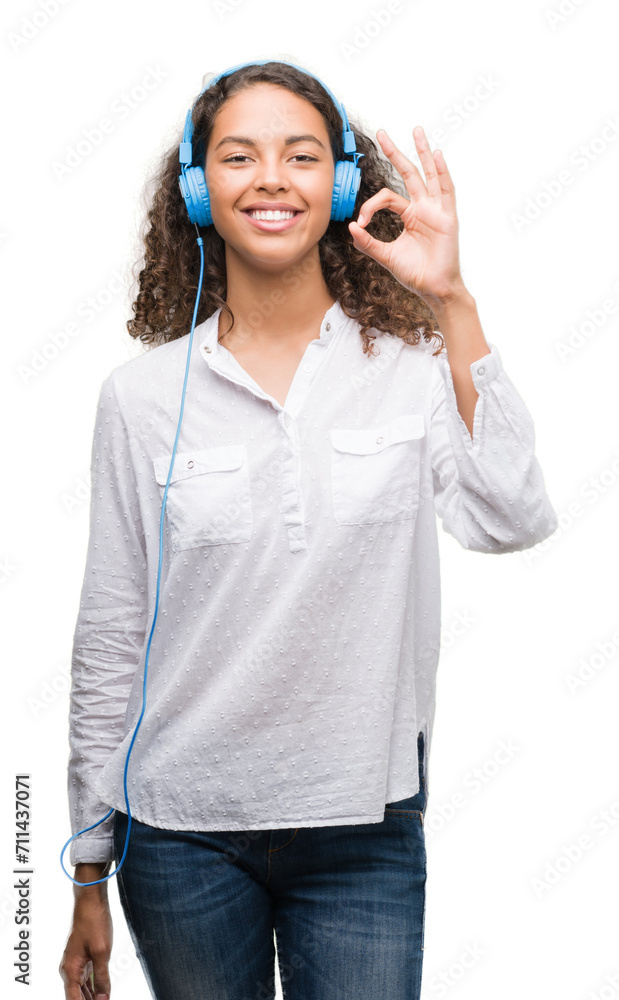 Young hispanic woman wearing headphones doing ok sign with fingers, excellent symbol