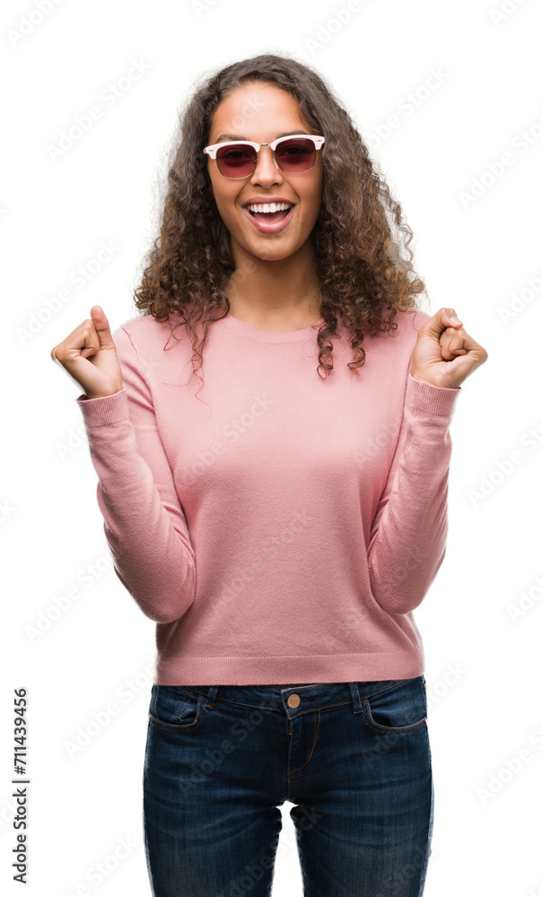 Beautiful young hispanic woman wearing sunglasses celebrating surprised and amazed for success with arms raised and open eyes. Winner concept. Beautiful young hispanic woman wearing sunglasses celebrating surprised and amazed for success with arms raised and open eyes. Winner concept.