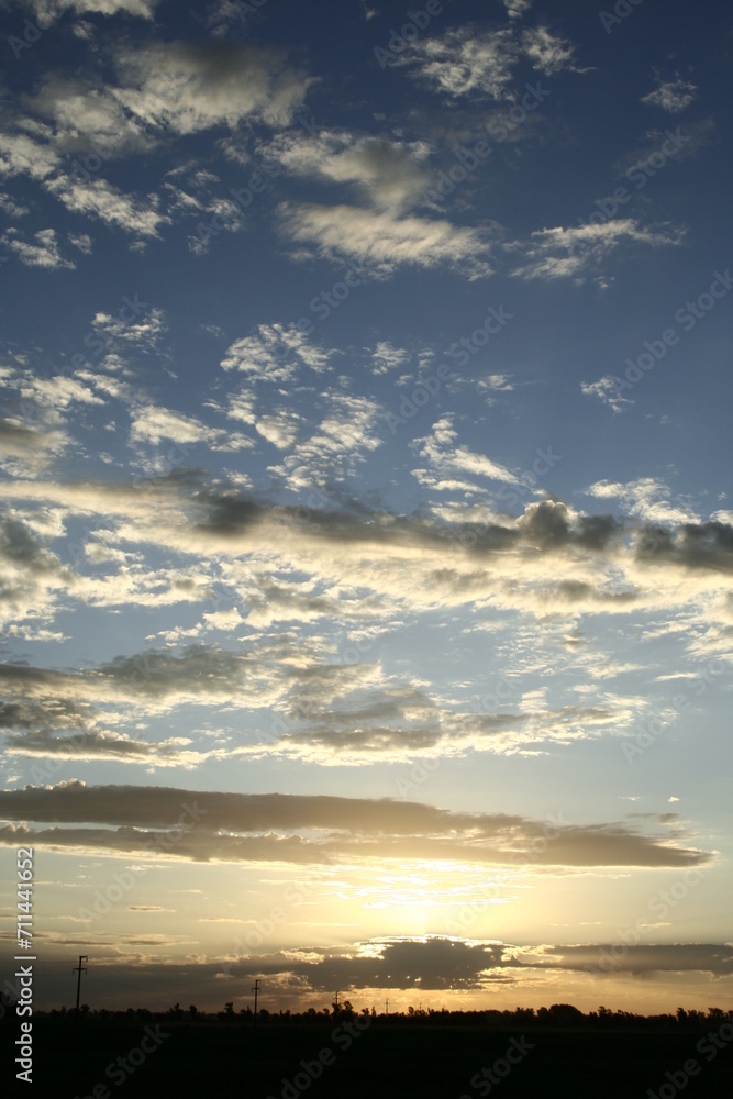 Atardecer en el campo de las Pampas sudamericanas, con nubes risadas y esponjosas y el sol cayendo en el horizonte, forma un original diseño natural con fondo del cielo azul