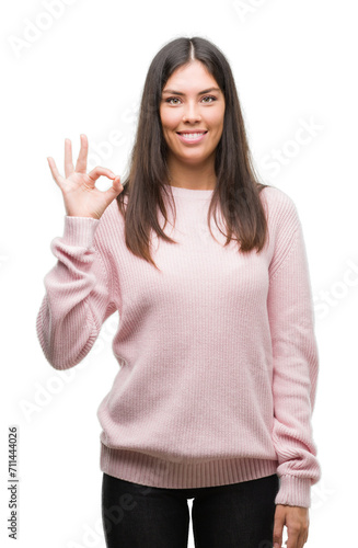 Young beautiful hispanic woman wearing a sweater smiling positive doing ok sign with hand and fingers. Successful expression.