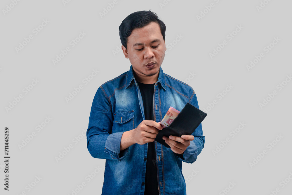 Young Asian man showing arrogant face expression while holding his wallet and counting the money Young Asian man showing arrogant face expression while holding his wallet and counting the money