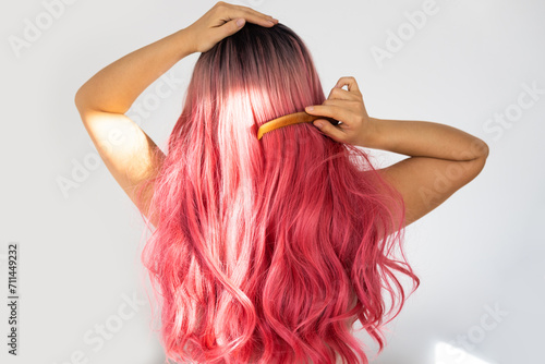 Rear view of a young beautiful woman with long pink curly hair combing her hair in the morning. Hair care concept.