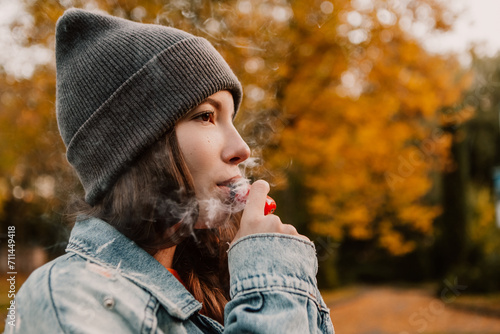 Canvas Print Young woman outside autumn park fall and smoking tobacco device electronic cigarette heater