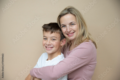 cool young teenager boy with white t-shirt posing together with his beautiful mother in front of brown background