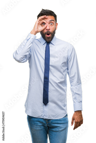 Adult hispanic business man over isolated background doing ok gesture shocked with surprised face, eye looking through fingers. Unbelieving expression.