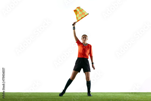 Stopping game. Young woman, soccer referee raising flag up meaning ball is out-of-play and game need restart against white background. Concept of sport, competition, match, profession, football game photo