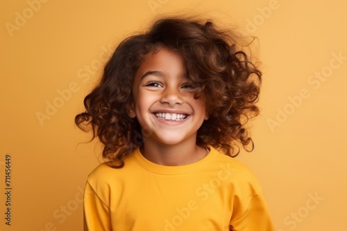 Portrait of a happy little girl with curly hair over yellow background
