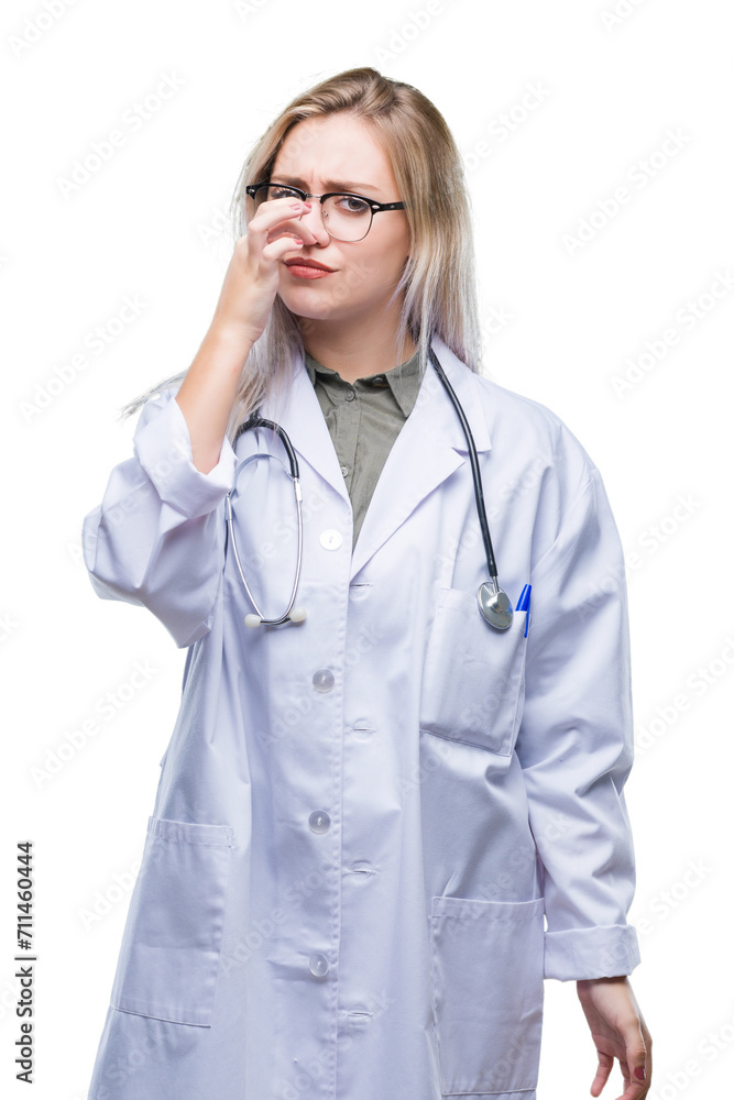 Young blonde doctor woman over isolated background smelling something stinky and disgusting, intolerable smell, holding breath with fingers on nose. Bad smells concept. Young blonde doctor woman over isolated background smelling something stinky and disgusting, intolerable smell, holding breath with fingers on nose. Bad smells concept.