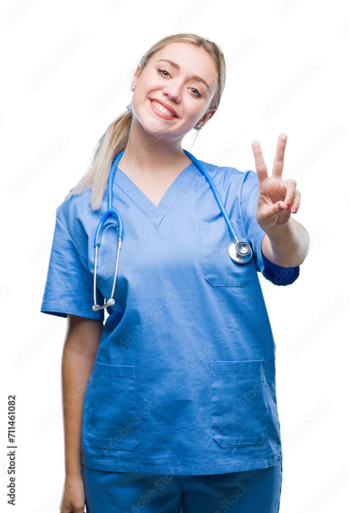 Young blonde surgeon doctor woman over isolated background smiling with happy face winking at the camera doing victory sign. Number two. Young blonde surgeon doctor woman over isolated background smiling with happy face winking at the camera doing victory sign. Number two.