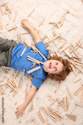 Cute little boy surrounded by wooden construction set on carpet at home, top view. Child`s toy