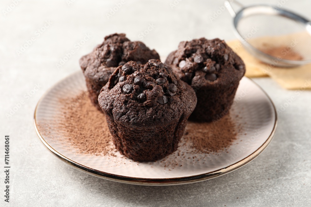 Delicious chocolate muffins and cacao powder on light grey table Delicious chocolate muffins and cacao powder on light grey table