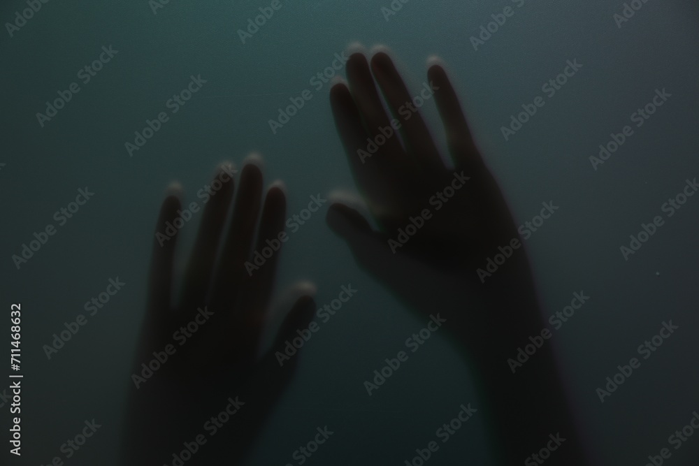 Silhouette of creepy ghost behind glass against color background, closeup
