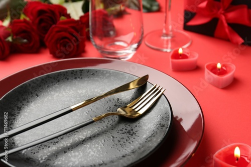 Place setting with heart shaped candles  gift box and bouquet of roses on red table  closeup. Romantic dinner