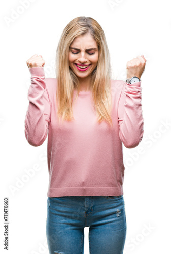 Young beautiful blonde woman wearing pink winter sweater over isolated background excited for success with arms raised celebrating victory smiling. Winner concept.