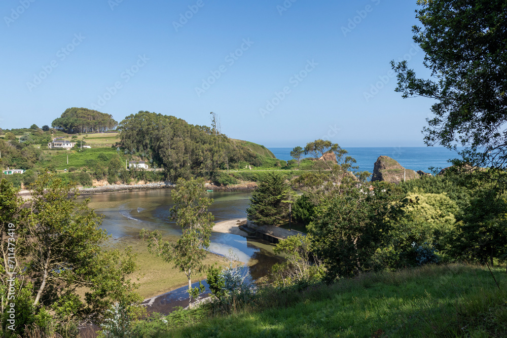 a serene bay with houses nestled in lush greenery, under a clear blue sky, with the open sea in the background
