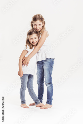 Studioportrait von zwei Schwestern Rücken am Rücken, barfuss in Jeans. Lächeln in die Kamera photo