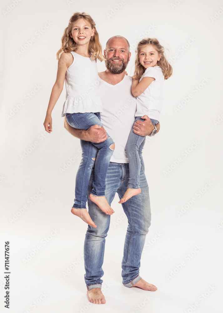 Studioportrait Vater mit Töchtern auf dem Arm barfuss in Jeans Studioportrait Vater mit Töchtern auf dem Arm barfuss in Jeans